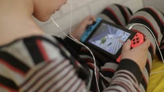 Ein 8-jähriger Junge spielt auf dem Bett ein Videospiel auf der Spielekonsole Switch.