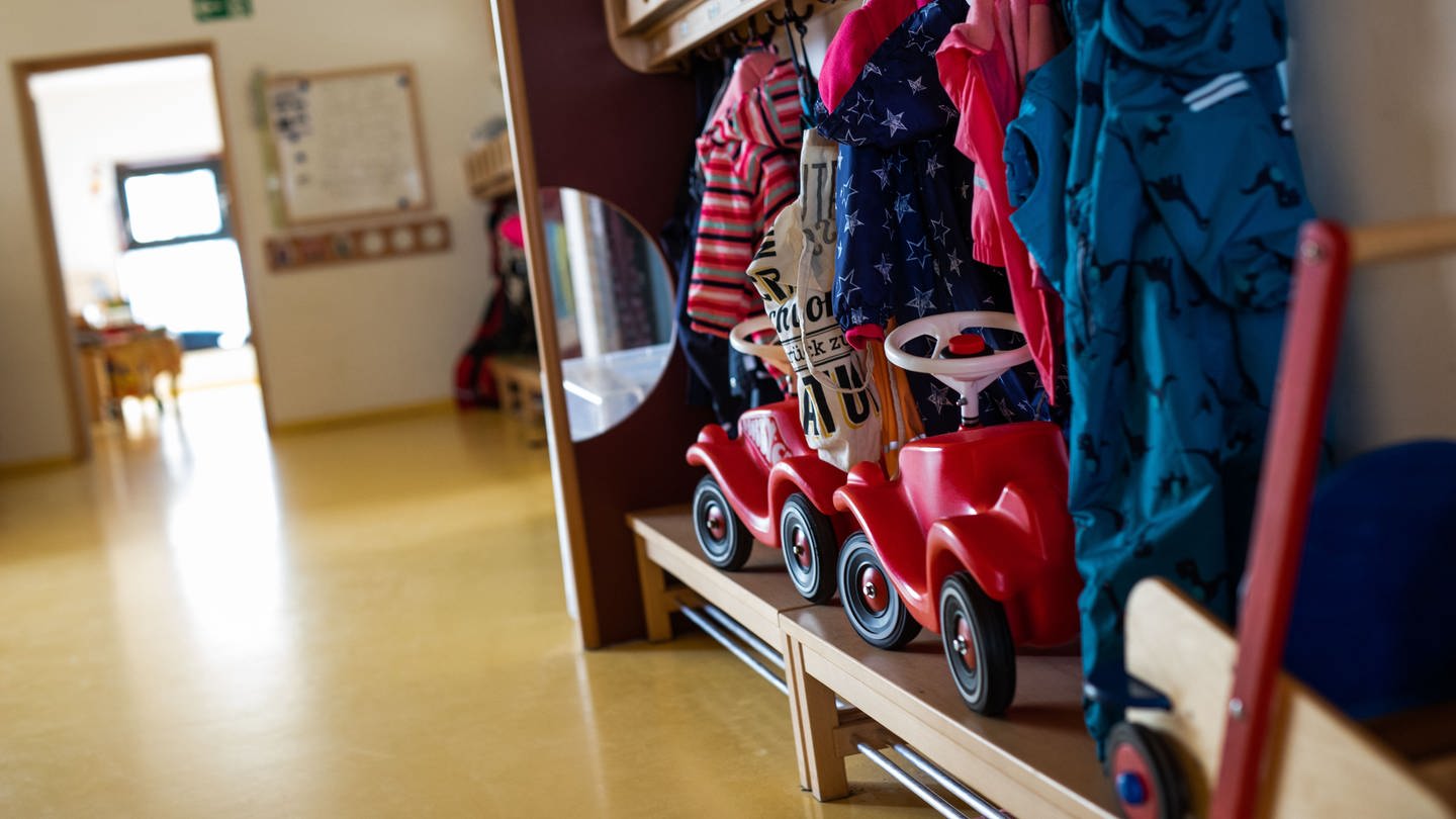 Bobbycars stehen unter Jacken von Kindern, die an einer Garderobe einer Kindertagesstätte (Kita) hängen.