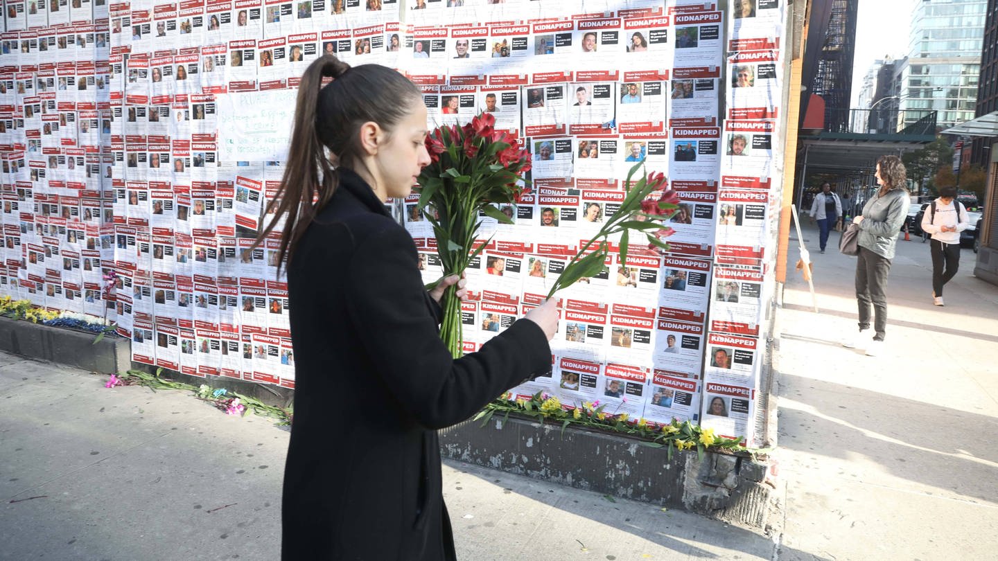 Frau legt Blumen vor die Wand mit den Bildern der israelischen Geiseln, die von der Hamas in den Gazastreifen entführt wurden.