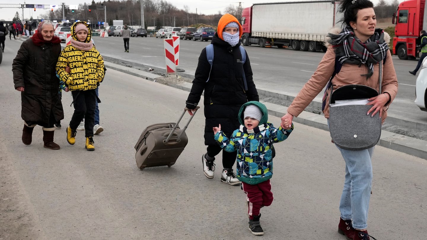 An einer Straße gehen Flüchtlinge aus der Ukraine entlang, es sind Frauen und Kinder.