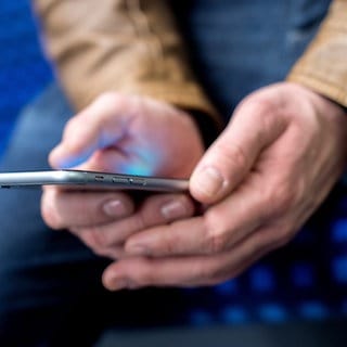 Ein junger Mann sitzt in einer S-Bahn und benutzt dabei sein Smartphone. 