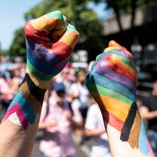 Zwei Teilnehmer der «Pride Berlin: Save our Community, Save our Pride» halten ihre Faust in die Höhe, die in Regenbogenfarbe angemalt sind.