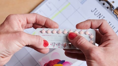 Über einem Kalender nimmt sich eine Frau die nächste Pille aus der Monatspackung der Antibabypille.