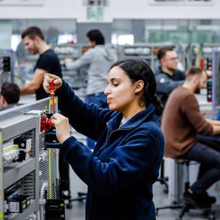 Eine junge Frau schraubt in einem Ausbildungsbetrieb der Metallindustrie an einer Tafel ein elektrisches Gerät fest.