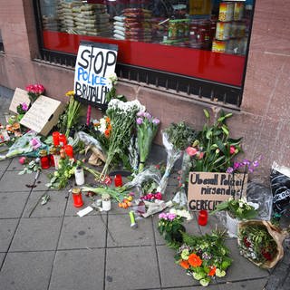 Blumen, Kerzen und Schilder liegen und stehen an dem Ort, an dem am Montag (02.05.2022) ein Mann nach einer Polizeikontrolle gestorben ist.