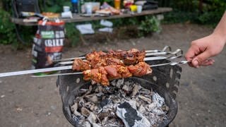 Ein Mann grillt im Park auf einem Grillplatz Fleischspieße.