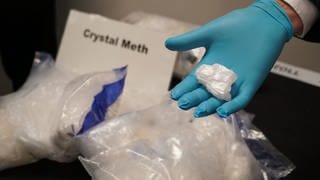 In Beuteln und auf einer Hand ist Crystal Meth zu sehen.