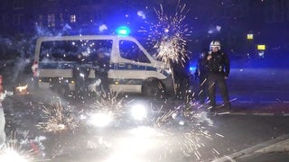 Polizeibeamte stehen hinter explodierendem Feuerwerk. Nach Angriffen auf Einsatzkräfte in der Silvesternacht hat die Diskussion um Konsequenzen begonnen.