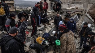 Syrische Zivilisten und Mitglieder der Weißhelme arbeiten an der Rettung von Menschen, die nach einem Erdbeben der Stärke 7,8 in Syrien unter einem zerstörten Gebäude eingeschlossen sind.