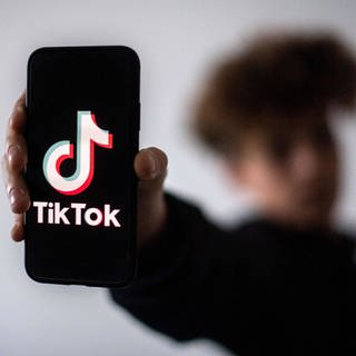 Ein Handy mit dem TikTok-Logo wird ins die Kamera gehalten