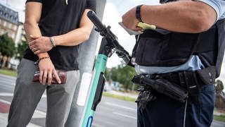 Bei einer Polizeikontrolle wird ein E-Scooter Fahrer von der Polizei verwarnt, weil er über einen Fußgängerweg gefahren ist.