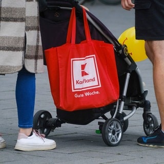 Eine Frau trägt an ihrem Kinderwagen eine Kaufland-Tüte.