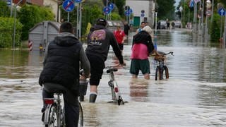 Ein Mann fährt auf einem Fahrrad eine überflutete Straße entlang. Die Region Emilia-Romagna kommt nach den Überschwemmungen nicht zur Ruhe.