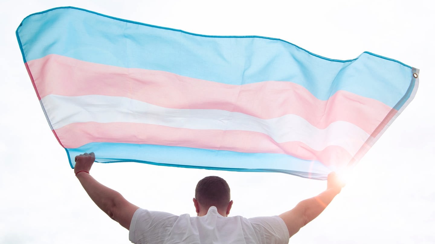 Ein junger Mann hält eine Trans-Pride-Flagge in die Luft