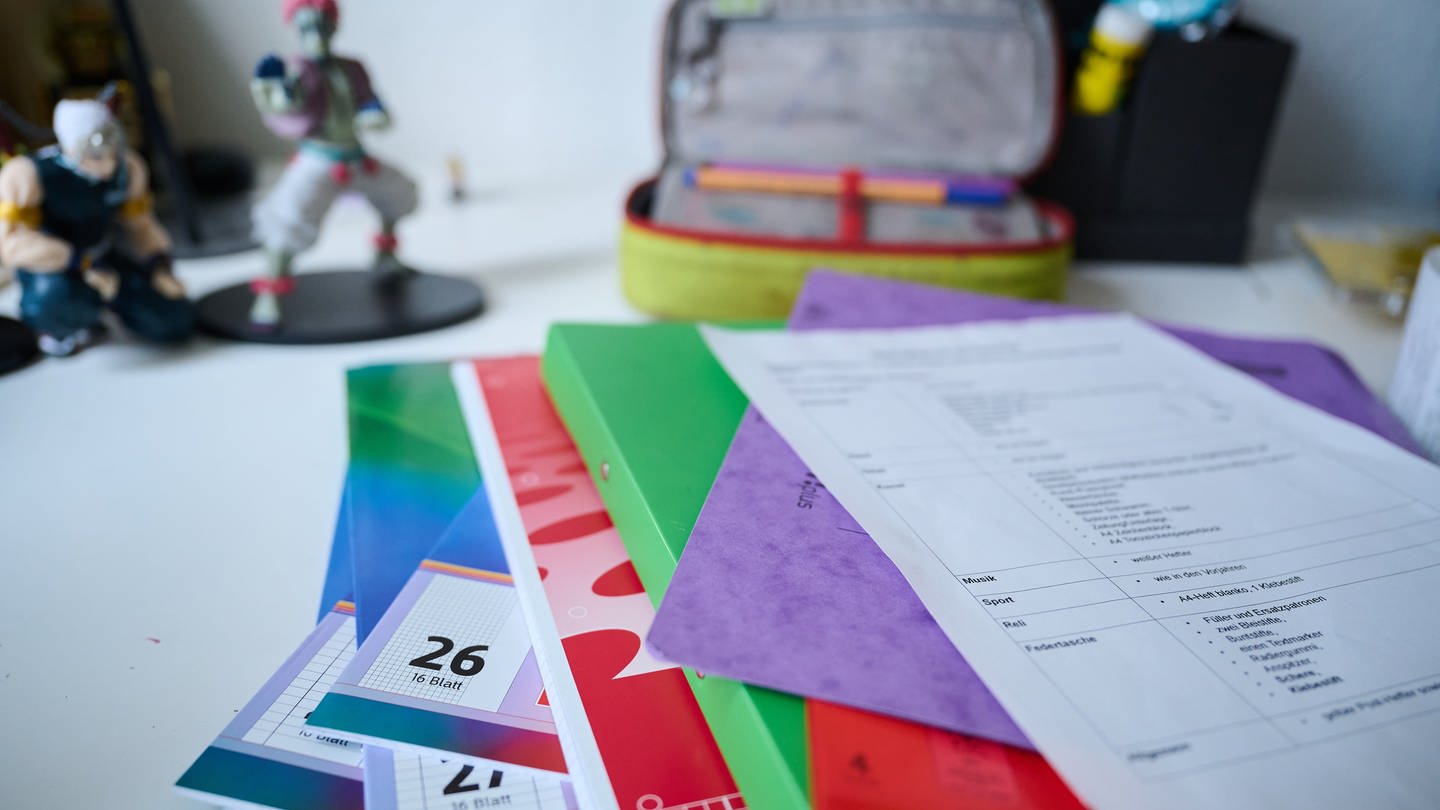 Symbolbild: Neue Schulhefte, Ordner und eine Materialliste für das neue Schuljahr liegen auf einem Kinderschreibtisch. Die Preise dafür sind deutlich gestiegen.