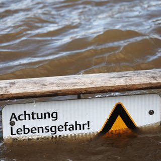 Ein Warnschild mit der Aufschrift "Achtung Lebensgefahr", das vor dem Schwimmen im Rhein warnt, ragt zum Teil aus dem Wasser. Bei Neuwied wollte ein Mann durch den Rhein schwimmen.