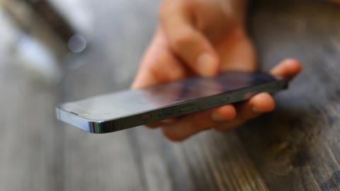 Ein junger Mann hält ein Smartphone (Symbolbild) In Spanien wurden Schülerinnen mit gefälschten Nacktbildern gemobbt