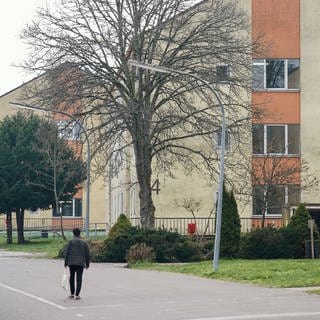 Ein Geflüchteter geht auf dem Gelände der Aufnahmeeinrichtung Kusel an Wohnhäusern vorbei. Hier sollen jetzt in einer neuen Halle mehr Menschen untergebracht werden.