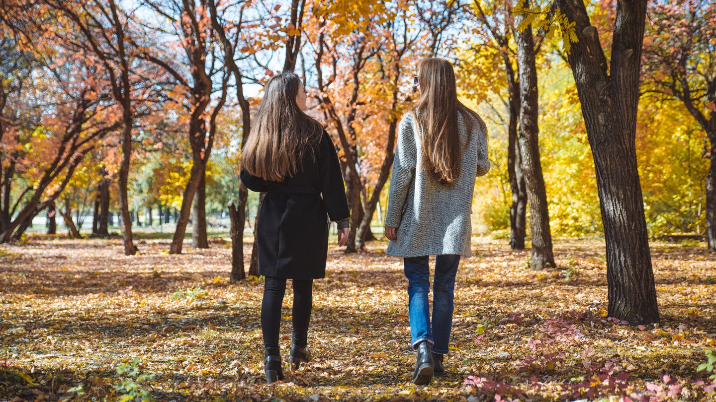 Zwei junge Frauen laufen durch einen Wald im Herbst.