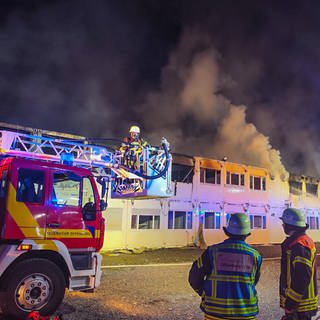 Feuerwehrleute löschen Feuer an einer Containerunterkunft. In einer Containerunterkunft für Flüchtlinge ist ein Feuer ausgebrochen. Mindestens 130 Menschen seien am Freitagabend evakuiert worden, teilte die Polizei mit.