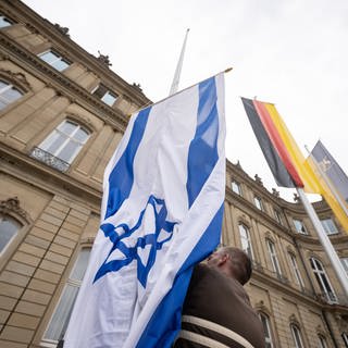 Die Flagge Israels wird von einem Mitarbeiter des Staatsministeriums Baden-Württemberg zwischen den Flaggen der EU, Deutschlands und Baden-Württembergs gehisst.