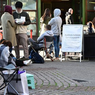 Menschen warten schon Stunden vor der Öffnung vor dem Eingang der Stuttgarter Ausländerbehörde. Die Wartezeiten sind in den letzten Monaten drastisch angestiegen.