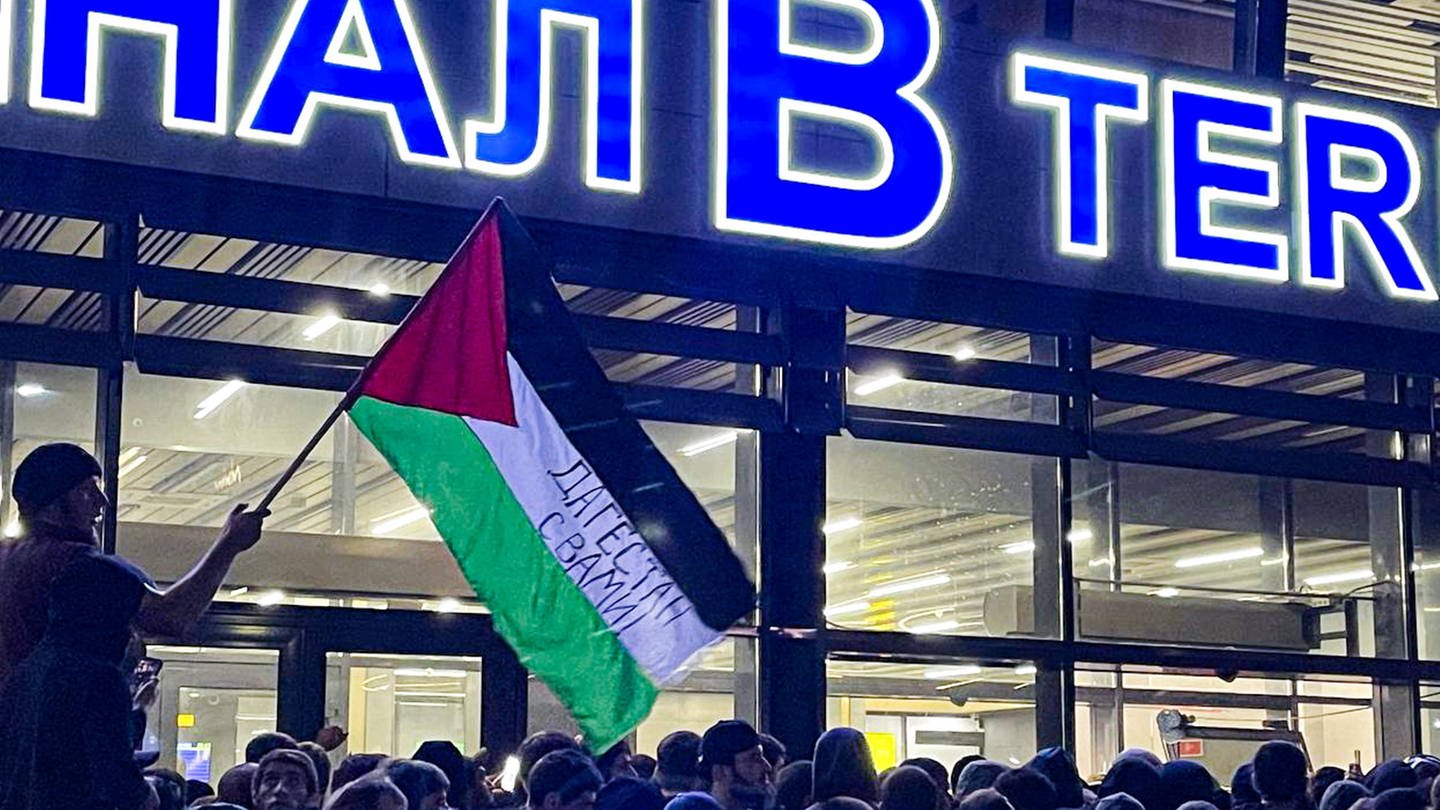 Ein wütender Mob vor dem Flughafen in Machatschkala, Dagestan. Eine Palestina-Flagge mit der Aufschrift 