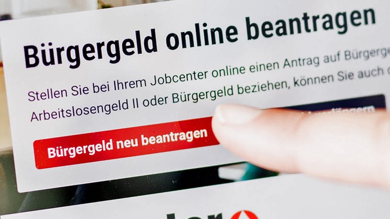 Eine Frau tippt auf einem Tablet auf einen Link zum Beantragen des Bürgergeldes im Kundenbereich im Jobcenter Berlin Mitte.