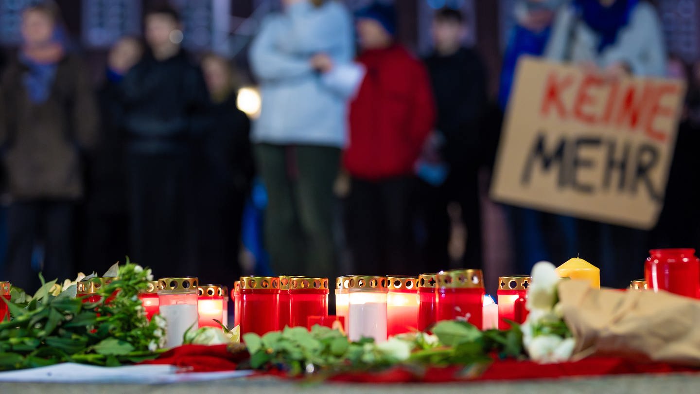 SYMBOLBILD: Menschen nehmen an einer Demonstration gegen Femizide teil und stehen dabei hinter niedergelegten Blumen und Kerzen.