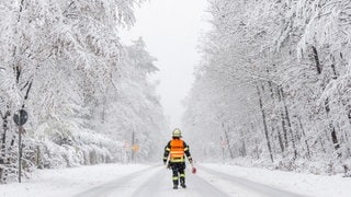 Ein Feuerwehrmann auf einer zugeschneiten Straße. In Wiesbaden sitzen Schüler wegen des Schnees in ihrer Schule fest.