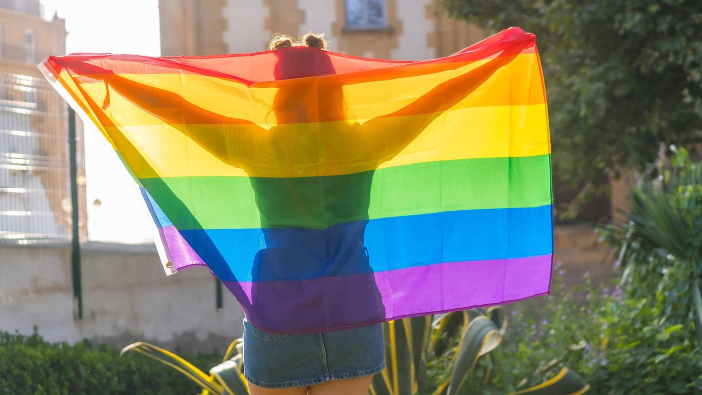 Frau von hinten mit einer Regenbogen-Flagge über den Schultern: In Russland ist die LGBTQ-Community als extremistisch verboten worden.