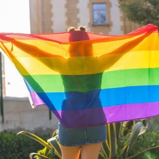 Frau von hinten mit einer Regenbogen-Flagge über den Schultern: In Russland ist die LGBTQ-Community als extremistisch verboten worden.