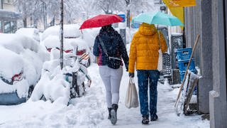 Zwei Menschen laufen mit Regenschirmen durch den tiefen Schnee in der Stadt. Der Schneefall ist aber kein Zeichen gegen den Klimawandel. 