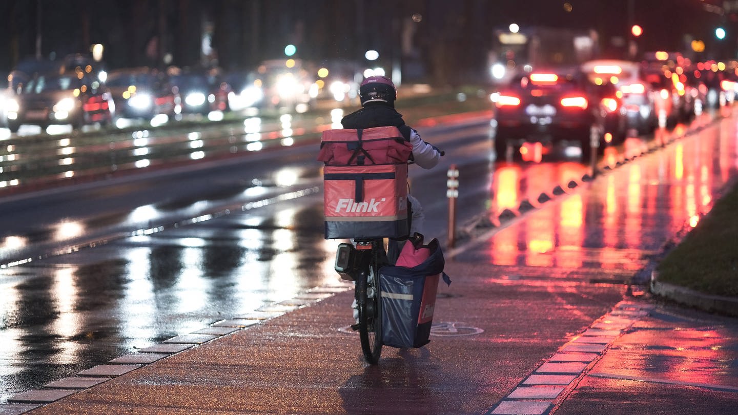 Lieferdienst-Fahrer von Flink unterwegs auf einer nassen Straße im Dunkeln: Die EU will die Rechte der Liefer- und Fahrdienste stärken.