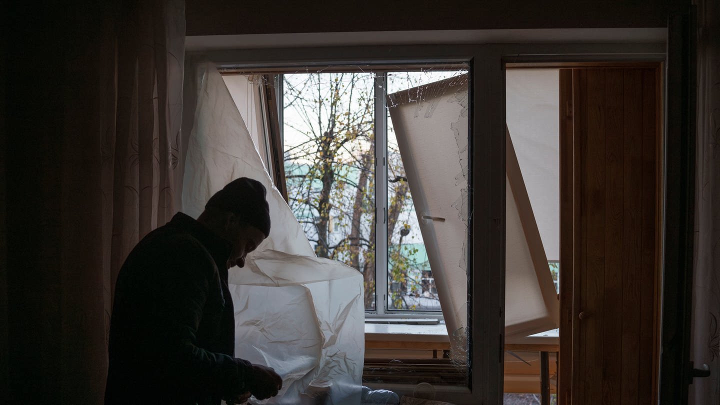 Ein Mann deckt ein zerbrochenes Fenster in seiner Wohnung nach einem russischen Drohnenangriff mit Plastik ab.