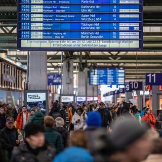 Während eine Anzeigetafel die aktuellen Abfahrten der Züge und den Hinweis auf mögliche Zugausfälle bezüglich des Sturms Zoltan anzeigt, laufen Reisende durch den Stuttgarter Hauptbahnhof.