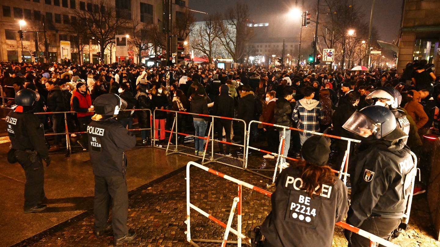 Polizisten stehen in der Silvesternacht 2021 hinter einer Absperrung am Brandenburger Tor, wo sich mehrere hundert Menschen versammelt haben.