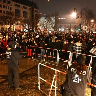 Polizisten stehen in der Silvesternacht 2021 hinter einer Absperrung am Brandenburger Tor, wo sich mehrere hundert Menschen versammelt haben.