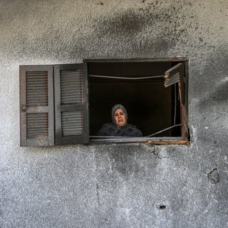 UN-Nothilfebüro OCHA "Gaza ist unbewohnbar geworden" - Frau schaut aus dem Fenster eines beschädigten Hauses in Gaza