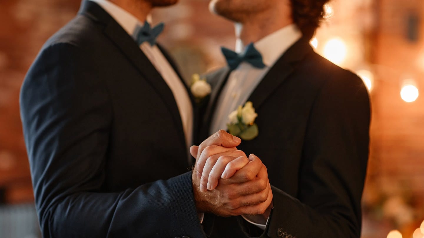 Zwei Männer tanzen zusammen auf ihrer Hochzeit und halten Händchen.