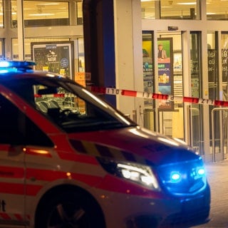 Ein Einsatzfahrzeug steht vor einem Supermarkt mit Blaulicht. Eine Frau wurde in dem Supermarkt erschossen. Der mutmaßliche Täter brachte sich danach selbst um.