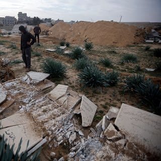 Palästinenser inspizieren beschädigte Gräber nach einem israelischen Panzerangriff auf einen Friedhof im Flüchtlingslager Chan Junis im südlichen Gazastreifen. (Symbolbild)