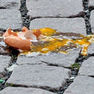 Geworfenes Ei, das kaputt gegangen ist, liegt auf einer Straße.