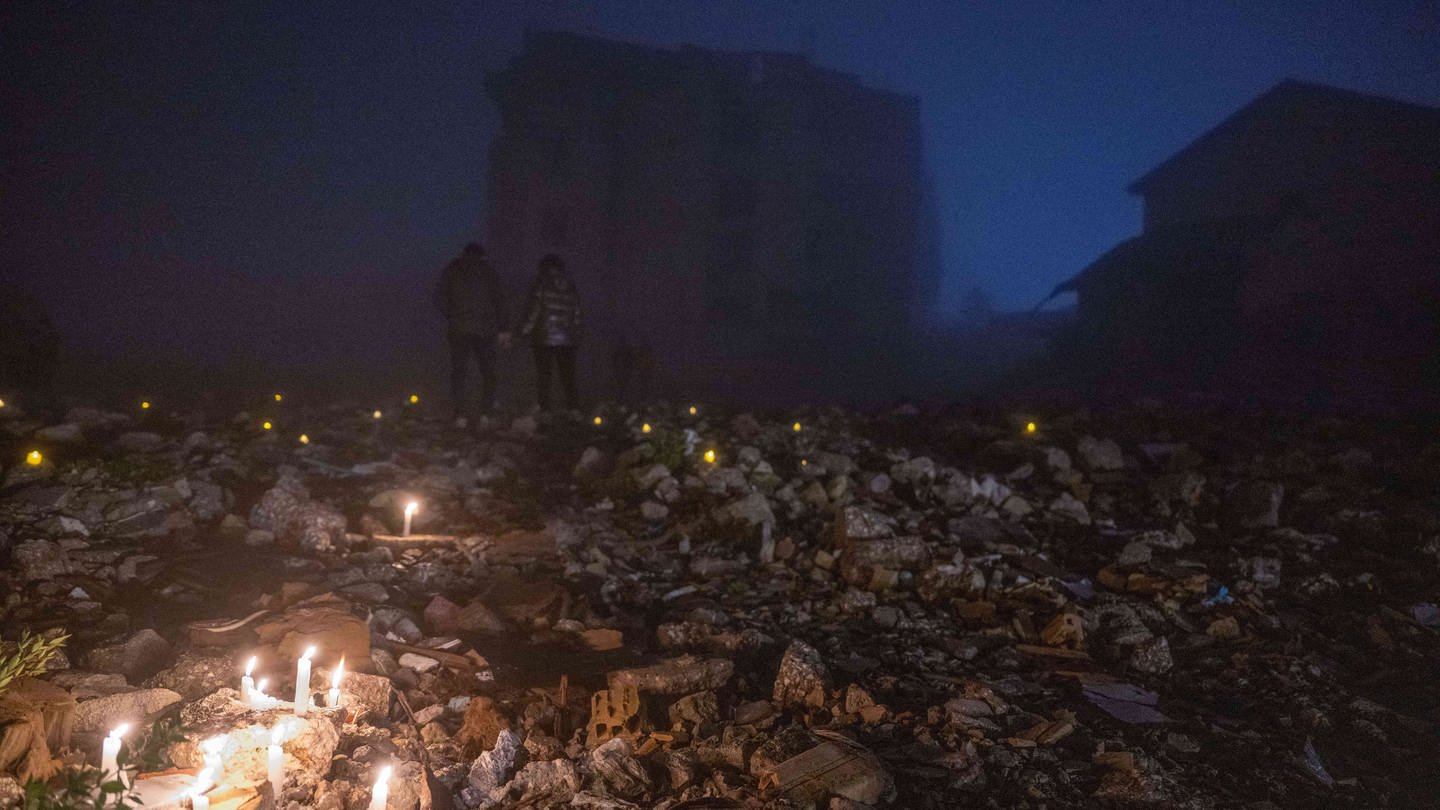 Mitten in der Nacht entzünden Menschen in den Trümmern eines beim Erdbeben zerstörten Hauses Kerzen, um an ihre Verwandten zu erinnern, die dort ums Leben gekommen waren. Vor einem Jahr hatten mehrere zehntausend Menschen bei einem massiven Erdbeben im Südosten der Türkei ihr Leben verloren. Bei der Trauerfeier gab es Buhrufe gegen die türkische Regierung.