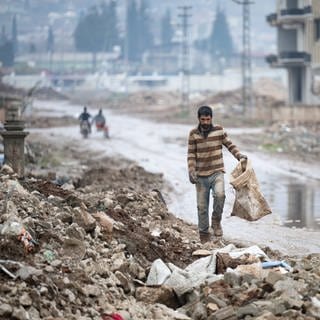 Ein Mann geht zwischen Trümmern und riesigen Wasserpfützen entlang zu seiner Behausung am Rande der Stadt. Im Zentrum der Stadt waren bei dem Beben vor einem Jahr zahlreiche Häuser zerstört oder massiv beschädigt worden.