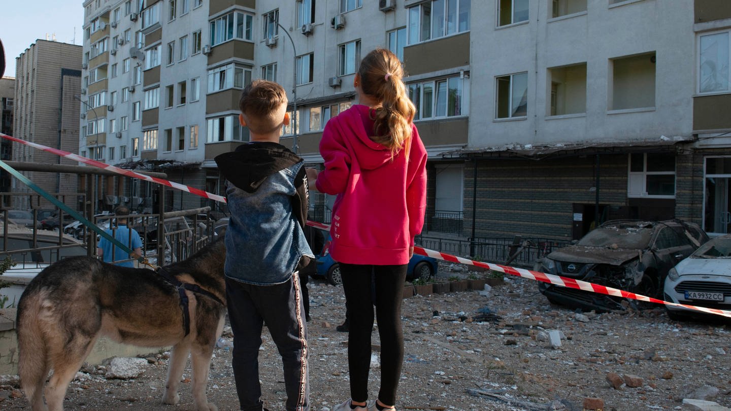 Kinder stehen vor einem beschädigten Gebäude in der Ukraine - Save the Children berichtet von über 600.000 Kindern in Not nach Rückkehr in die Ukraine