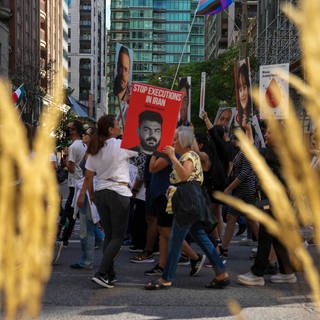 Eine junge Frau hält ein Banner mit dem Bild von Saman Yasin, einem Rapper, der seit Protesten 2022 inhaftiert ist, die durch den Tod von Mahsa Amini ausgelöst wurden.