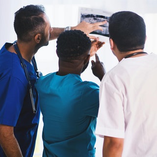 Drei Mediziner schauen sich Befunde eines Patienten an.