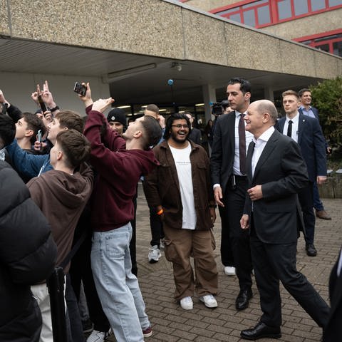 Bundeskanzler Olaf Scholz (SPD, r) geht während eines Besuchs der Gottlieb-Daimler-Schule über den Schulhof und lässt sich von Jugendlichen fotografieren.