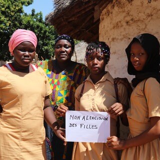 In September 2022, Koulako, 39, poses with her daughters and a sign that reads ‘No to the excision of girls’, at their home in the commune of Damaro in the Kankan region of Guinea.